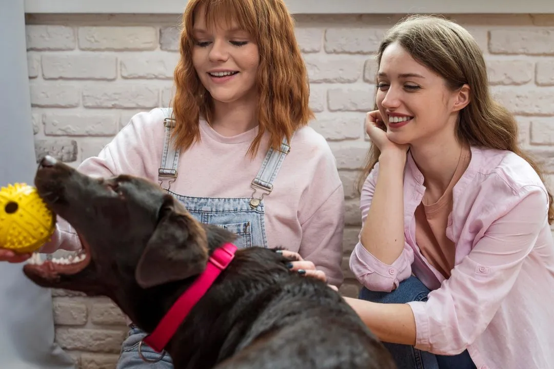 Two women sitting on a couch petting a dog.